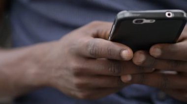 Siyah adamın elleri akıllı telefondan yazı yazıyor. Yakın çekim.