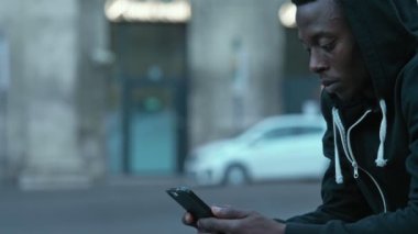 Smartphone'da yazarak sokakta oturan siyah Afrika genç adam