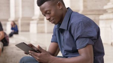 merdivenlerde oturan tablet kullanarak mutlu rahat siyah Afrika delikanlı