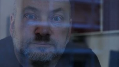 Pencerenin cam, arkasında dalgın hayalifener olgun adam kameraya bakıyor