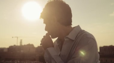Pensive adam elektronik sigara içme ve şehirde gün batımı nı düşünüyor