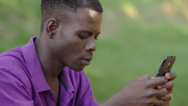 若いアフリカ系アメリカ人の男性がスマートフォンで入力しています コミュニケーション — ストック動画
