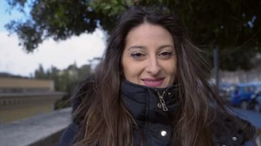 Gülümseyen rahat sevimli esmer kamera bakıyor- rüzgarlı gün- yavaş hareket