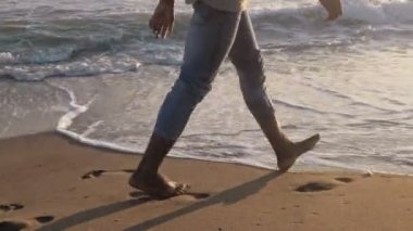 Siyah Afrikalı adam gün batımında sahilde yürüyor.