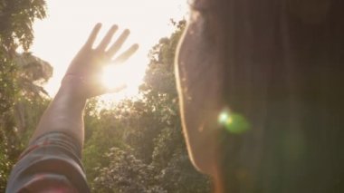Young woman raising up her hands to the sun in park-slow motion