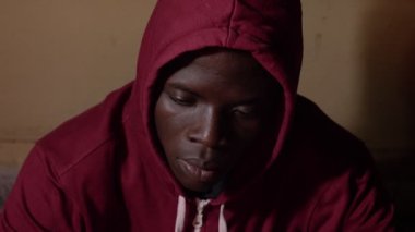 Üzgün gururlu yalnız genç kapüşonlu Afrikalı adam karanlıkta yalnız, kameraya bakıyor