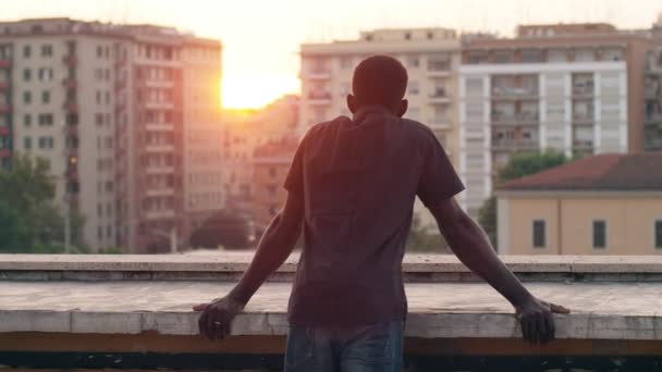 孤独的非洲男子在屋顶上看着日落的城市后视图 — 图库视频影像