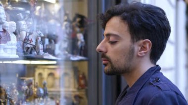Noel alışveriş portresi: genç adam hediyeler arayan bir dükkanın penceresi gözlemler