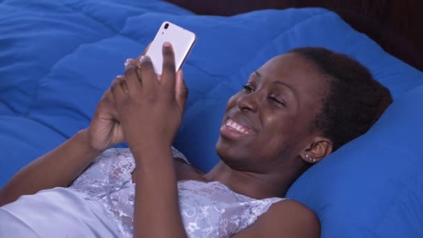 Glücklich Schwarzafrikanische Frau Mit Smartphone Auf Dem Bett Der Früh — Stockvideo