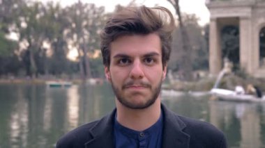 Ciddi bir genç adam gölün kenarındaki kameraya bakıp gülmeye başladı.