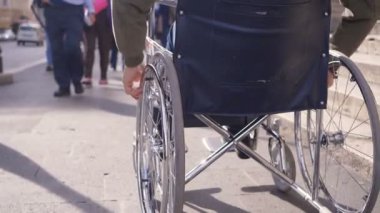 Genç engelli bir adamın eli kaldırımda tekerlekli sandalyesini itiyor.