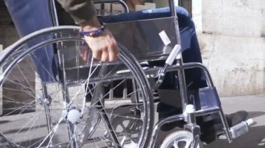 Genç engelli bir adamın eli kaldırımda tekerlekli sandalyesini itiyor.