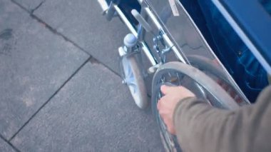 Genç engelli bir adamın eli kaldırımda tekerlekli sandalyesini itiyor.