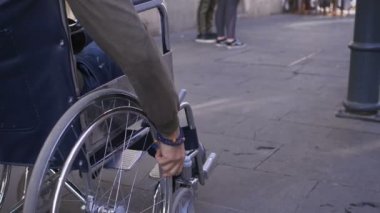 Genç engelli bir adamın eli kaldırımda tekerlekli sandalyesini itiyor.