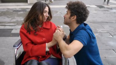 Handikap, aşk, romantizm. Tekerlekli sandalyedeki genç kadın çekici bir adamla flört ediyor.