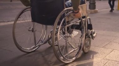 Genç engelli bir adamın eli kaldırımda tekerlekli sandalyesini itiyor.
