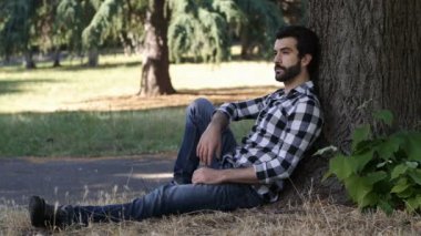 Genç adam parkta çimlerin üzerinde oturuyor.