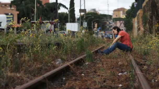 可怜的年轻人坐在铁轨上 — 图库视频影像