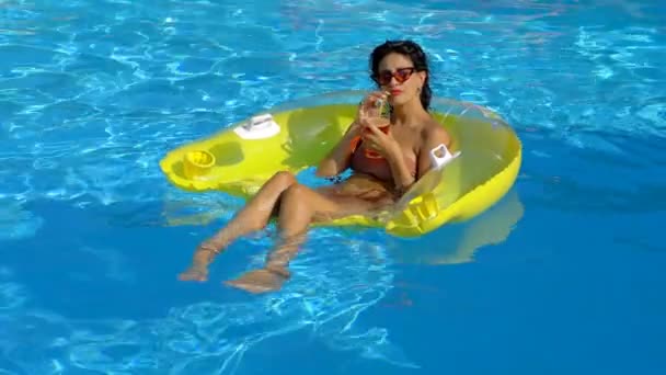 若い美しい女性がカメラで微笑むプールのインフレータブルでリラックスし — ストック動画