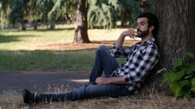 Genç adam parkta çimlerin üzerinde oturuyor.