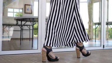 Yüksek topuklu giyen zarif bir kadının bacakları pencerenin önünde yürüyor.