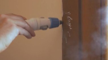 Kapı çerçevesindeki boya lekelerini silmek için buharlı temizleyiciyi tutan işçi eli.