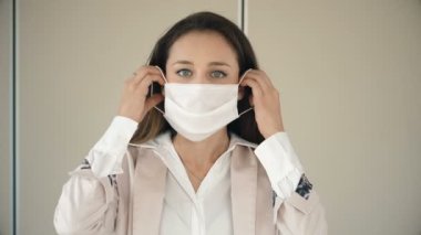 Cerrahi maske takan genç bir iş kadını kameraya bakıyor.