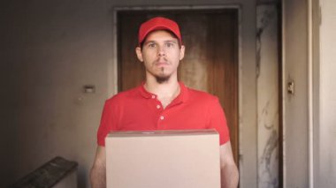 Genç kurye elinde kameraya gülümseyen bir paket tutuyor.