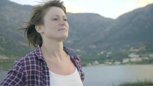 Young woman standing on top of a cliff on an island looking at the ocean. Sunset — Stock Video