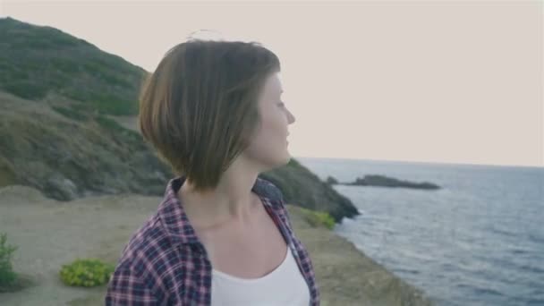 Jeune femme debout au sommet d'une montagne et regardant la mer. Coucher de soleil — Video