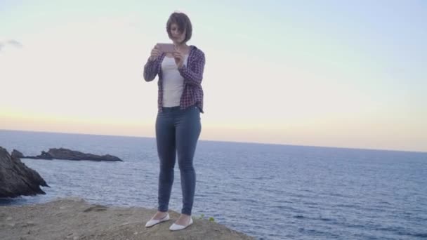 山の上に立っている若い女性がかかる写真海。サンセット — ストック動画