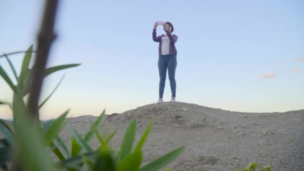 Νεαρή γυναίκα να στέκεται στην κορυφή ενός βουνού λαμβάνει εικόνες στη θάλασσα. Ηλιοβασίλεμα. Ελλάδα. Κρήτη. — Αρχείο Βίντεο