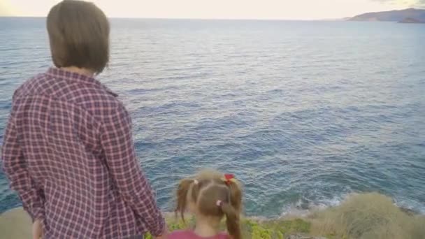 Madre e hija de pie en la cima de una montaña y mirando al mar. Puesta de sol — Vídeos de Stock