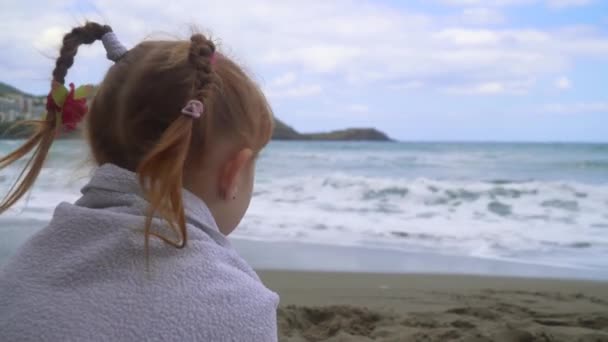 Kleine meisje zitten op het strand en kijk naar zee. — Stockvideo