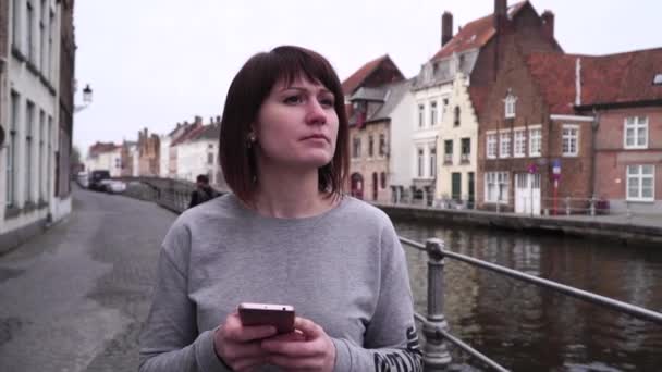 Lány Turisztikai séták, nézte a térképet a smartphone, és úgy néz ki, a látnivalók, a város Bruges Belgiumban. lassú mozgás — Stock videók