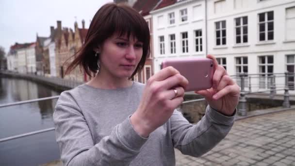 Mujer turista toma fotos en el teléfono inteligente en Brujas Bélgica. cámara lenta — Vídeos de Stock