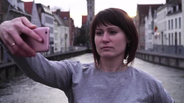 Дівчина туристичних робити selfie на смартфон на заході сонця в Брюгге, Бельгія. повільний рух — стокове відео