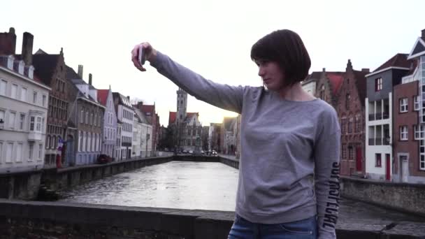 Chica turista haciendo selfie en el teléfono inteligente al atardecer en Brujas Bélgica. cámara lenta — Vídeo de stock