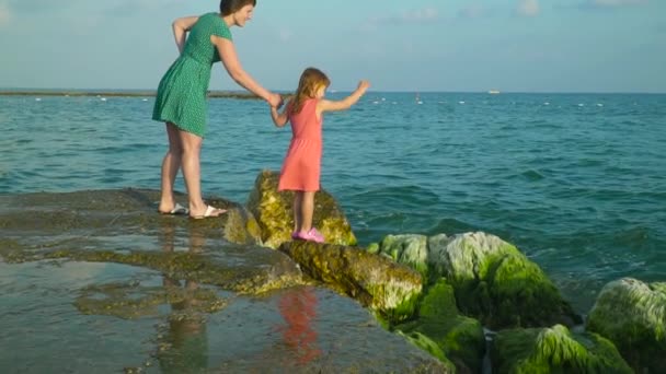 Mom and daughter standing on wet rocks in seawater with splashing waves around having fun. Slow Motion — Stock Video
