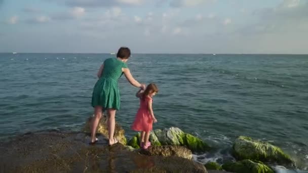 Woman with girl on rocks in waves — Stock Video