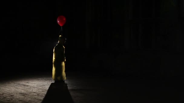 Silhouette masculine en manteau jaune avec ballon rouge à la main dans l'obscurité — Video