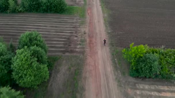 Повітряний постріл Молодий чоловік їде на велосипеді по сільській дорозі через фермерські землі — стокове відео