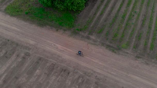 Letecký záběr mladý muž na kole na kole na venkovské silnici přes zemědělské půdy — Stock video