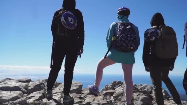 Turistas de pie en la cima de la montaña y mirando al mar por debajo, vista trasera — Vídeos de Stock