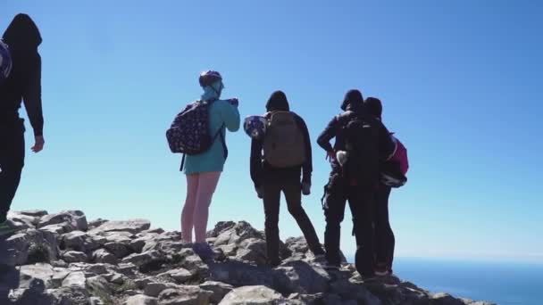 Turistas se acercan en la cima de la montaña y mirando al mar por debajo, vista trasera — Vídeos de Stock