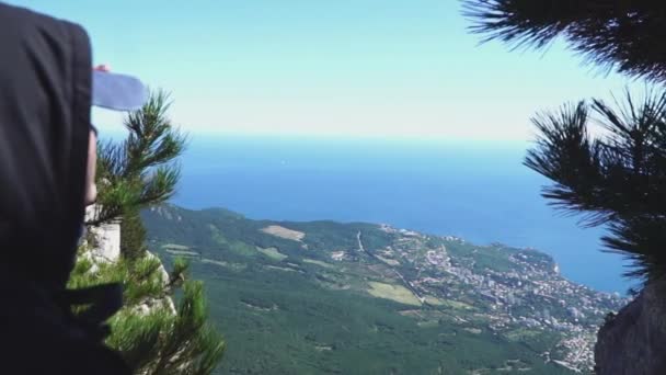 Persona en la cima de la montaña y mira al mar, vista trasera — Vídeos de Stock