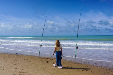 Yalnız bir kadın güzel bir güneş ve deniz gününde iki olta kamışı arasındaki denizi düşünür.