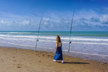 Yalnız bir kadın güzel bir güneş ve deniz gününde iki olta kamışı arasındaki denizi düşünür.