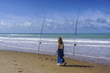 Yalnız bir kadın güzel bir güneş ve deniz gününde iki olta kamışı arasındaki denizi düşünür.