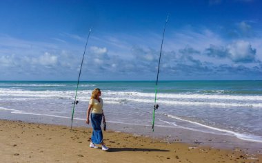 Yalnız bir kadın güzel bir güneş ve deniz gününde iki olta kamışı arasındaki denizi düşünür.